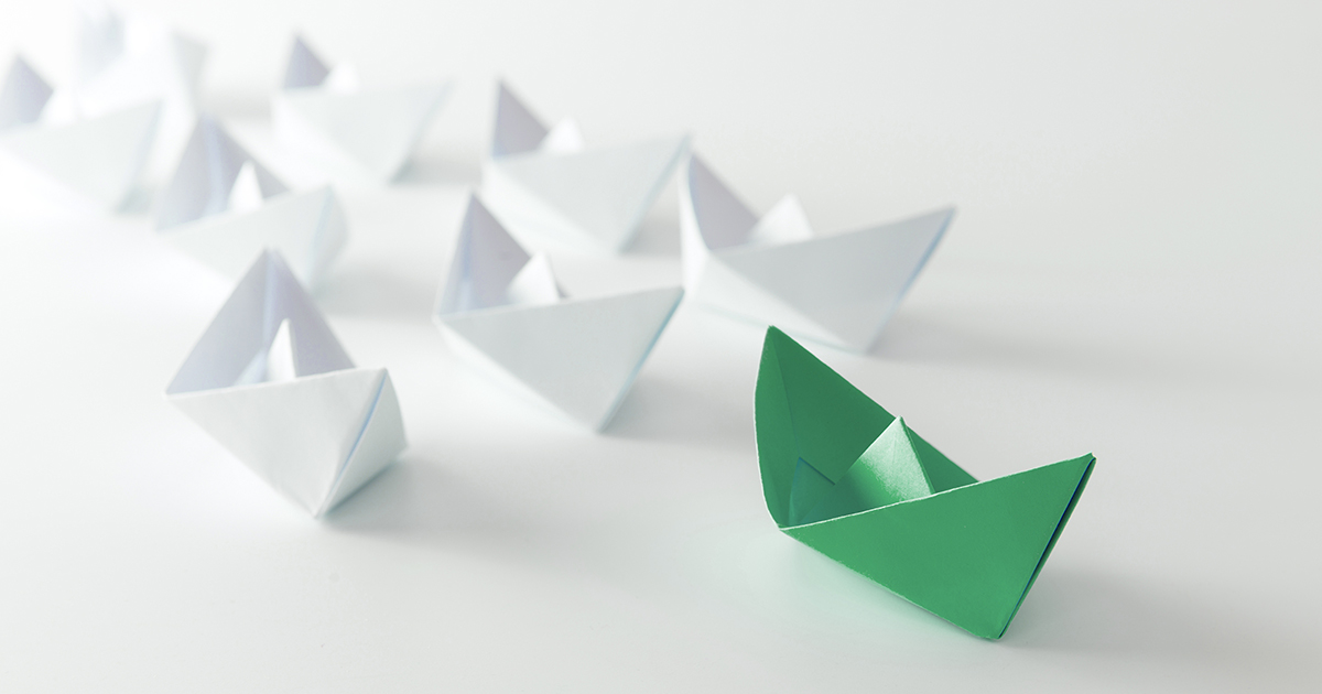 A green paper boat leads a fleet of white paper boats