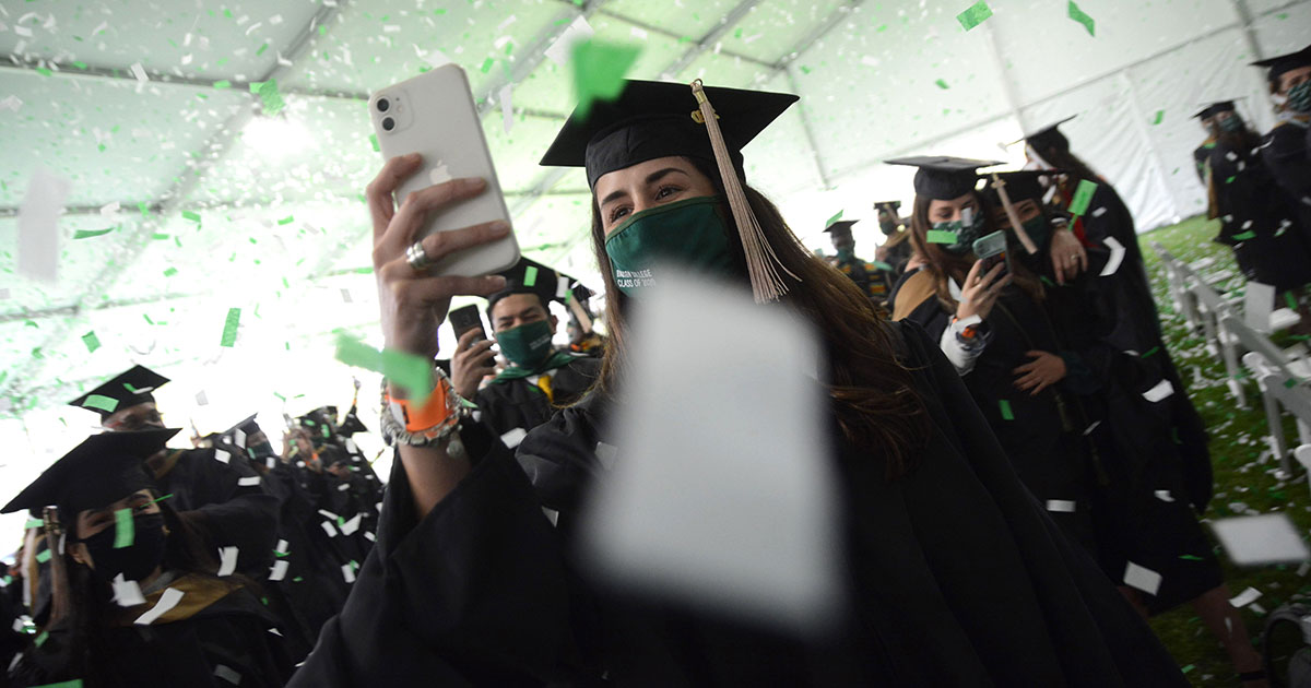 Student takes a picture as confetti falls at Class of 2020 commencement