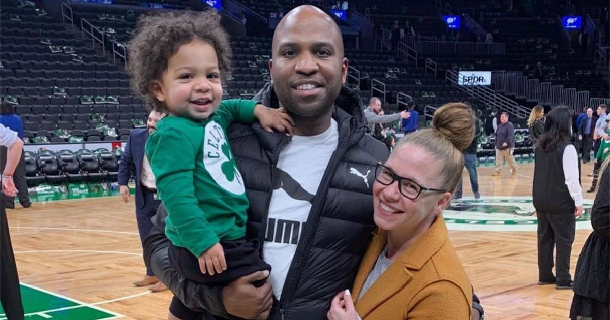 Mackenzie Silverio Henderson ’00 stands with her husband, Jermaine, and son, Tyler, on the basketball court at TD Garden