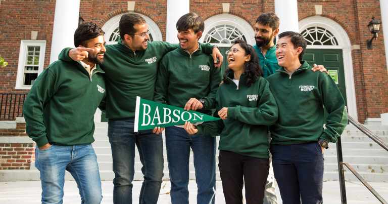 Graduate students pose with a Babson pennant