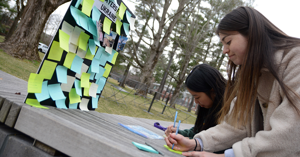 Students write post-it notes to put on a board of Prayers for Ukraine