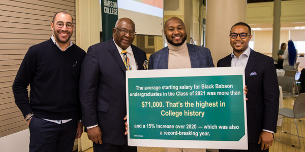 Four alumni pose for a photo with a sign touting the starting salary for Black Babson undergraduates in the Class of 2021