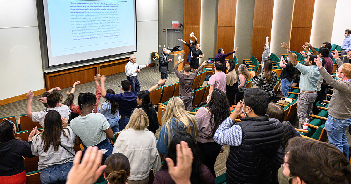 Students in an auditorium wave their arms to John Lennon's song "Imagine" during Babson's traditional last lecture