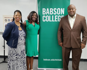 Three people stand on either side of a Babson College banner