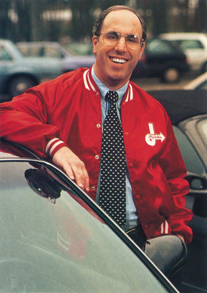 Stephen Spinelli poses in a red Jiffy Libe jacket while standing next to a car