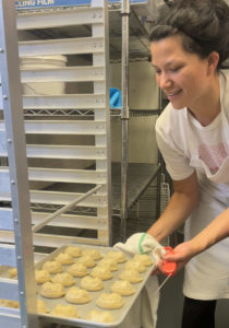 A female chef places a tray of dumplings on a kitchen rack.