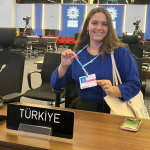 Ela Gokcigdem displays her COP27 badge while sitting at a table with a sign that reads, "Turkiye"