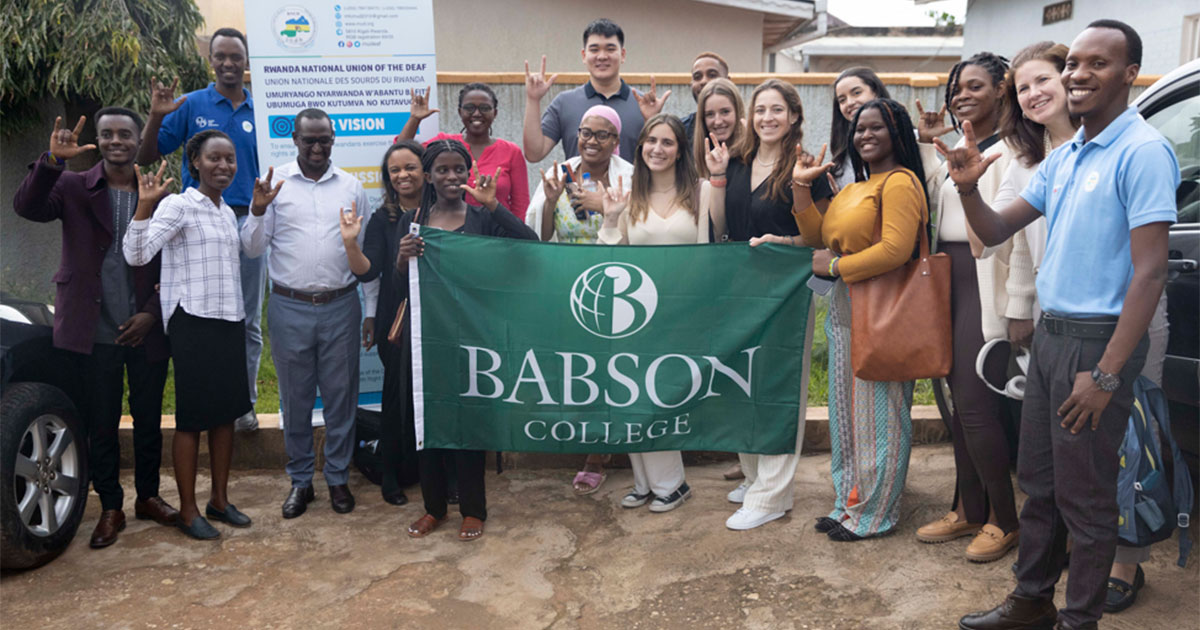 A group of people stands, posing for the camera, with some holding a Babson flag