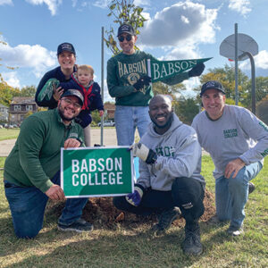 Alumni hold a Babson sign and pennant while posing for a photo