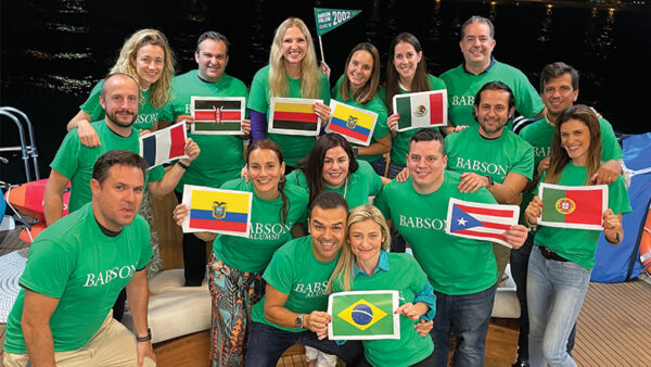 Alumni hold various country flags while posing for a photo during their trip
