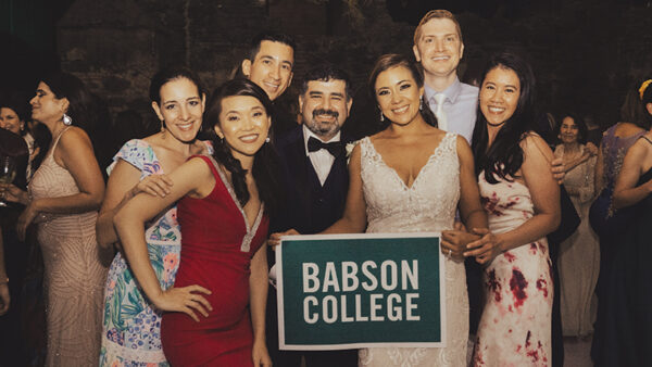 Claudia Gutierrez ’09 and Mario Chui pose for a photo with friends while holding a Babson sign