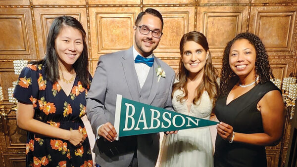 Miguel Vázquez Jr. and Angela Grace Colantonio pose for a photo with friends while holding a Babson pennant