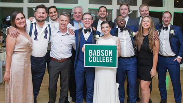 Brian Lawler and Sarah Anthony pose for a photo with friends while holding a Babson sign