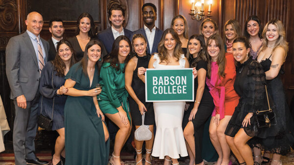Maria Bravo poses for a photo with friends while holding a Babson sign