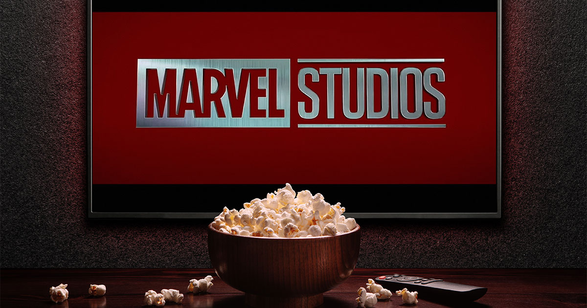 Popcorn and a remote control rest on a table in front of a TV screen that reads Marvel Studios