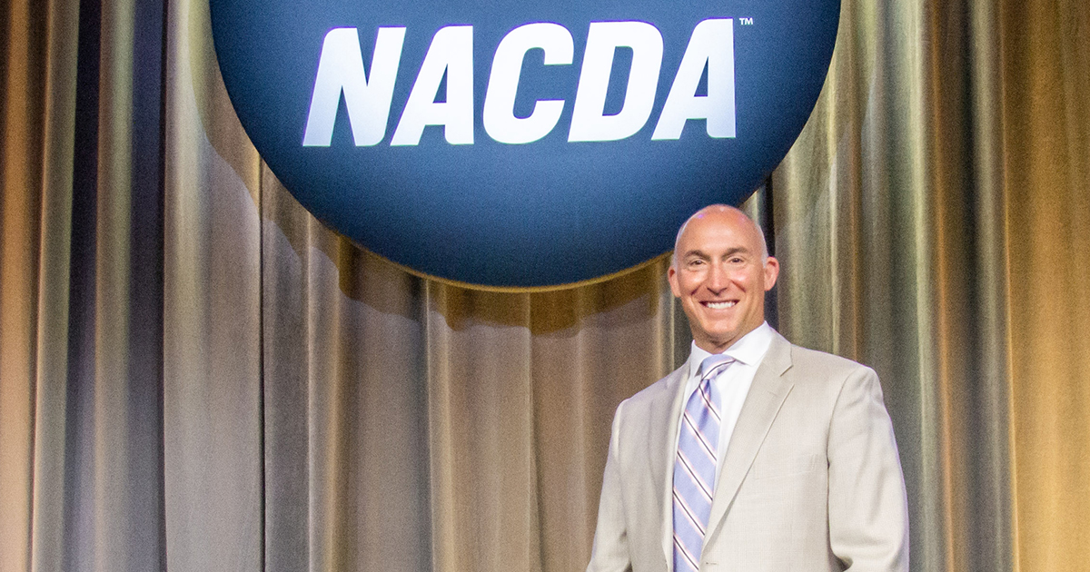 Mike Lynch poses in front of the NACDA logo
