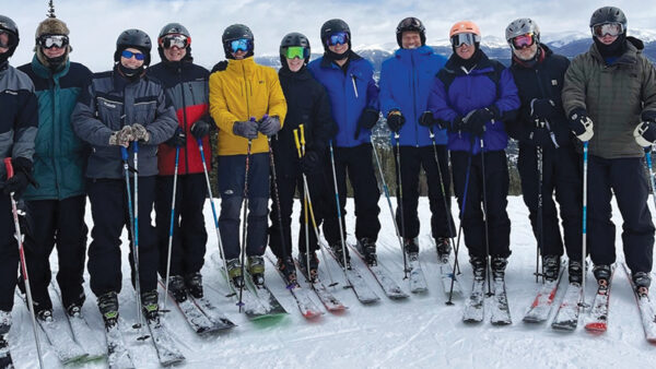 Alumni in ski gear stand in a line for a group photo on the slopes