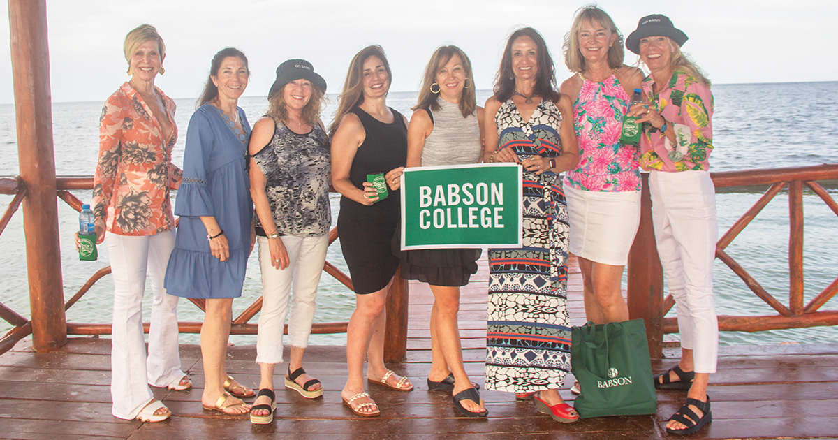 A group of women pose for a photo while standing and holding a Babson banner