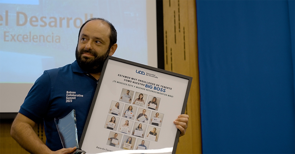 Carlos Varela stands on stage and holds an award and framed gift from his team members.