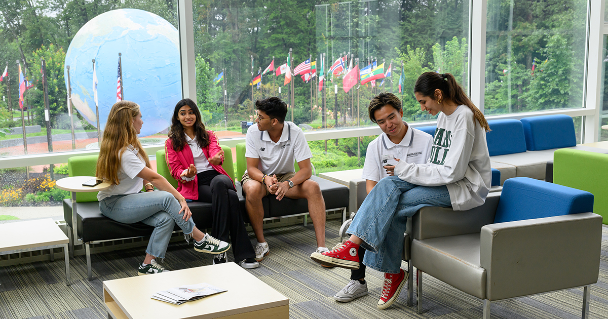 A group of five students sit in discussion in a space overlooking the Babson World Globe