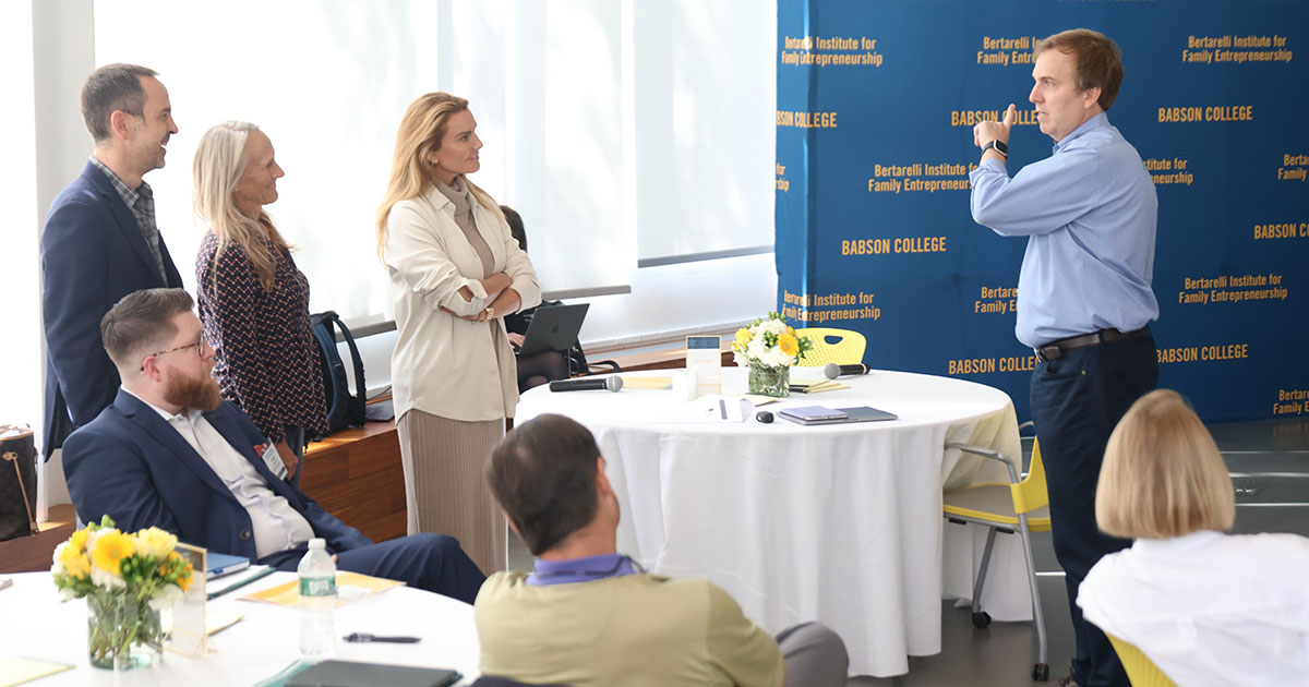 People sit and stand around tables, listening to a speaker at an event of the Global Family Entrepreneurship Network