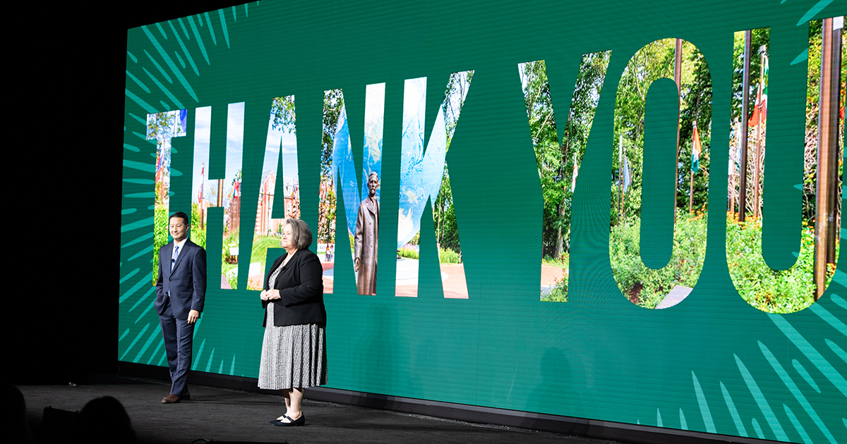 Speakers stand on stage in front of a giant Thank You message