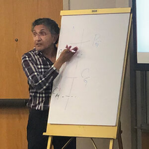 A professor motions to a white board while teaching