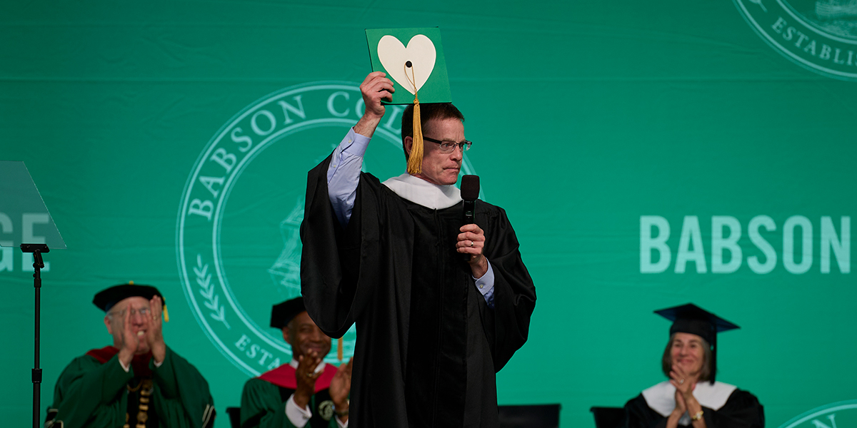 Tim Ryan holding up a graduation cap with a heart on it while on stage