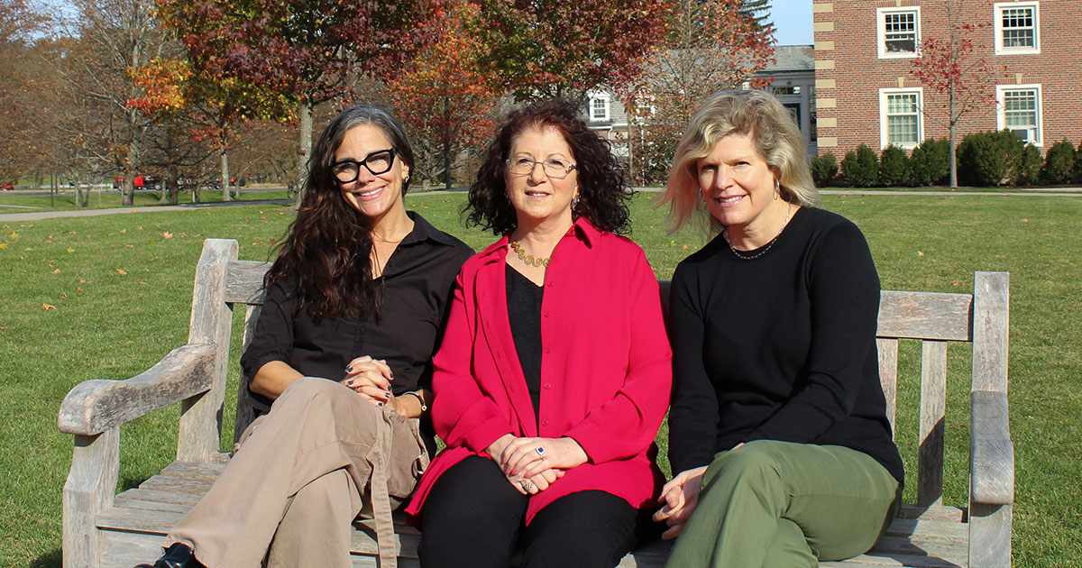 Three women sit on a bench on Babson’s campus