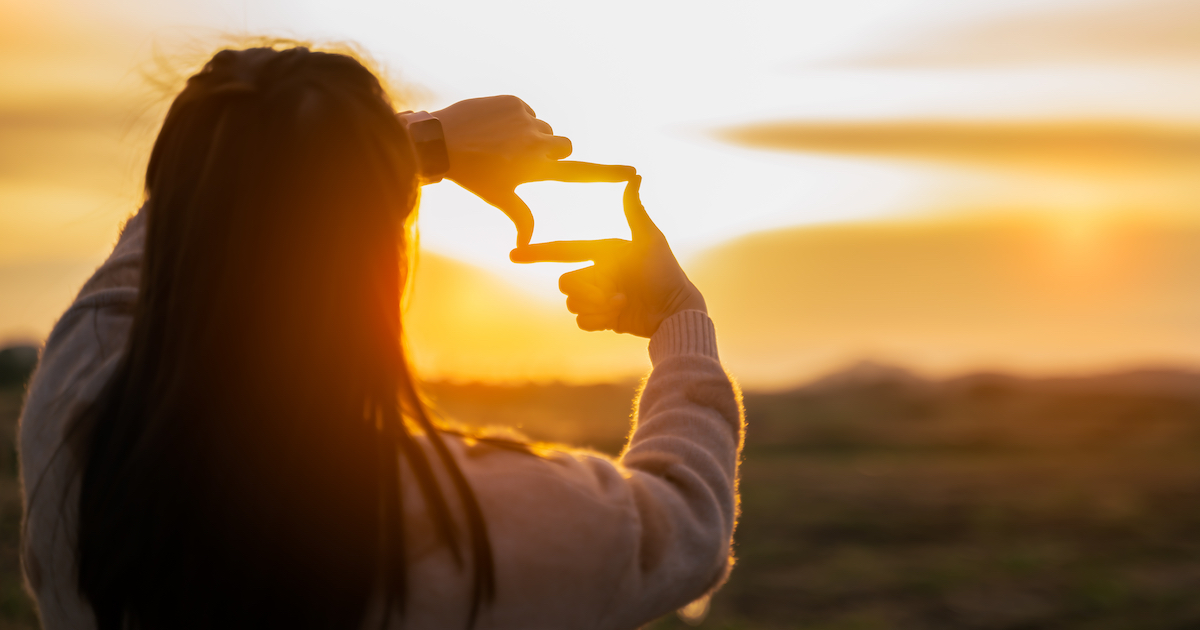 Photo of woman making frame round with her hands over a sunset.