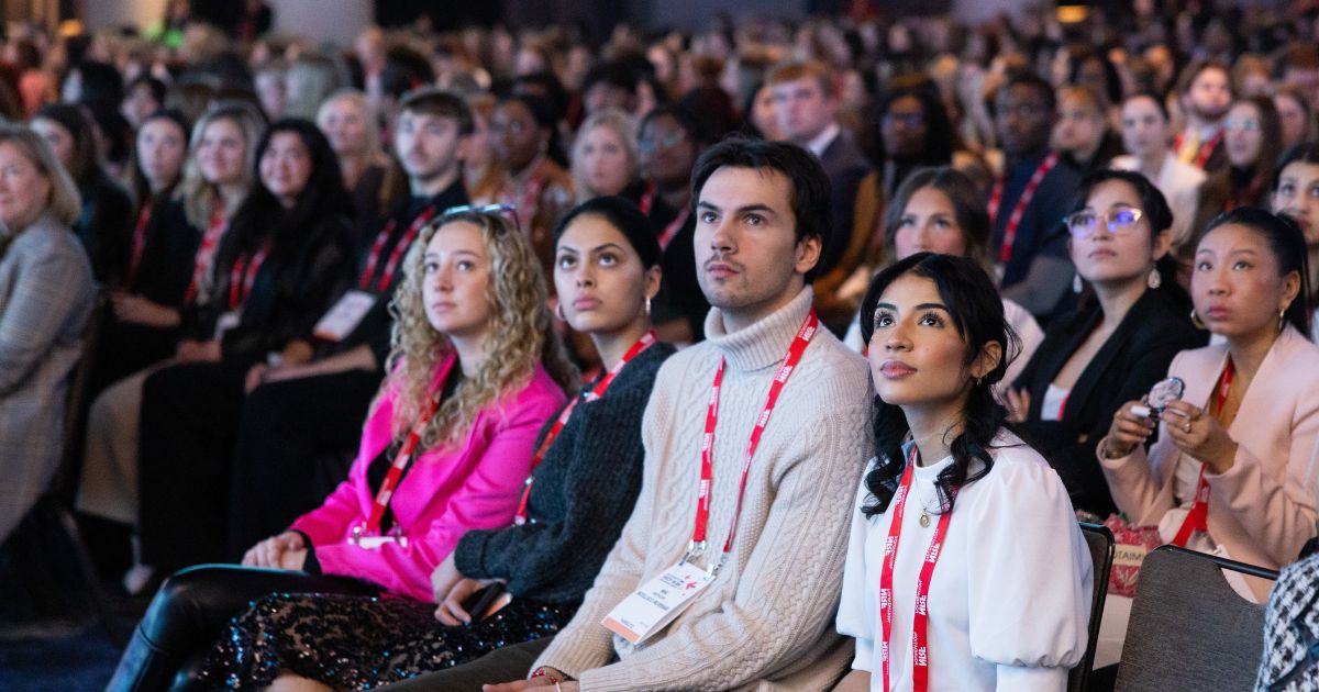 Four Babson students sit in a theater full of conference attendees