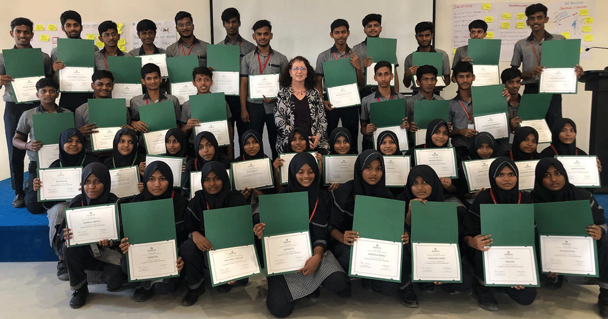 Babson’s Beth Goldstein sits in the middle of rows of students holding up certificates