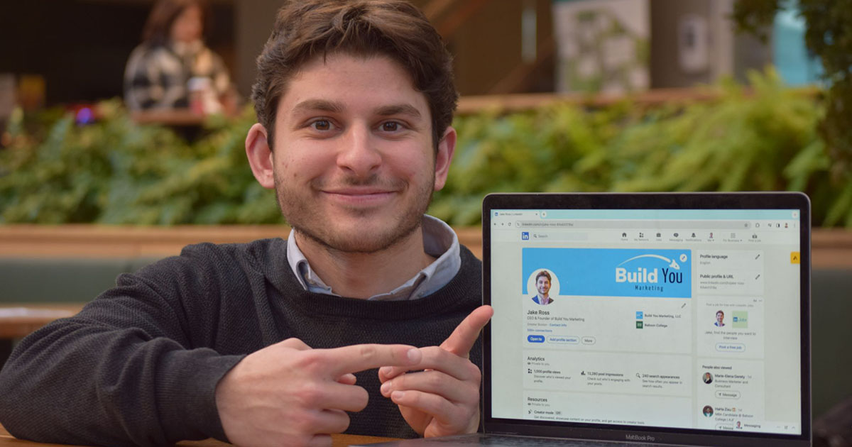 Jake Ross poses for a photo while pointing to a screen with his venture's website