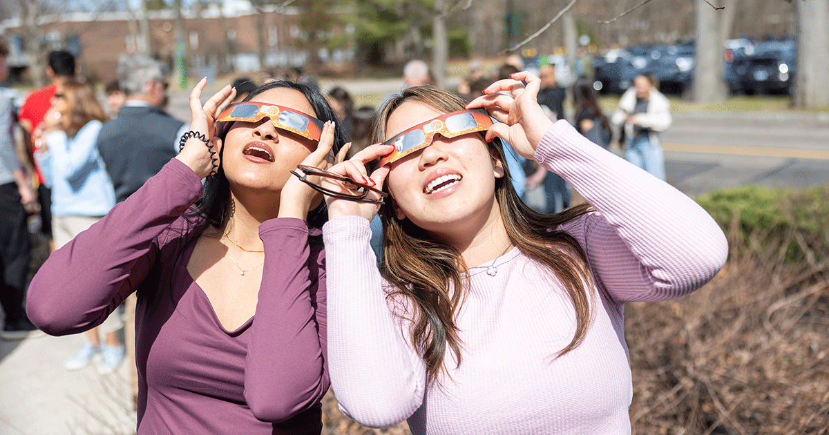 Two students wearing protective eyeglasses look up to the sky to see the solar eclipse