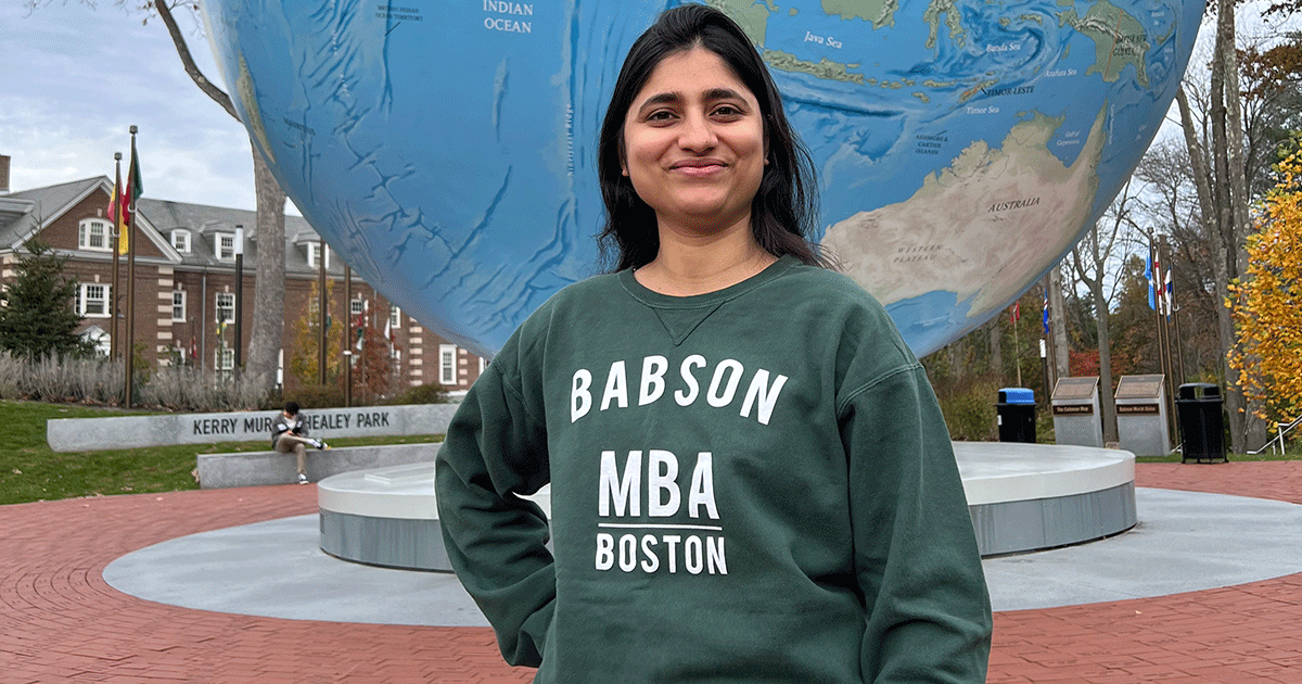 Shilphi Chaudhary MBA’24 stands in front of the Babson World Globe while wearing a Babson MBA sweatshirt