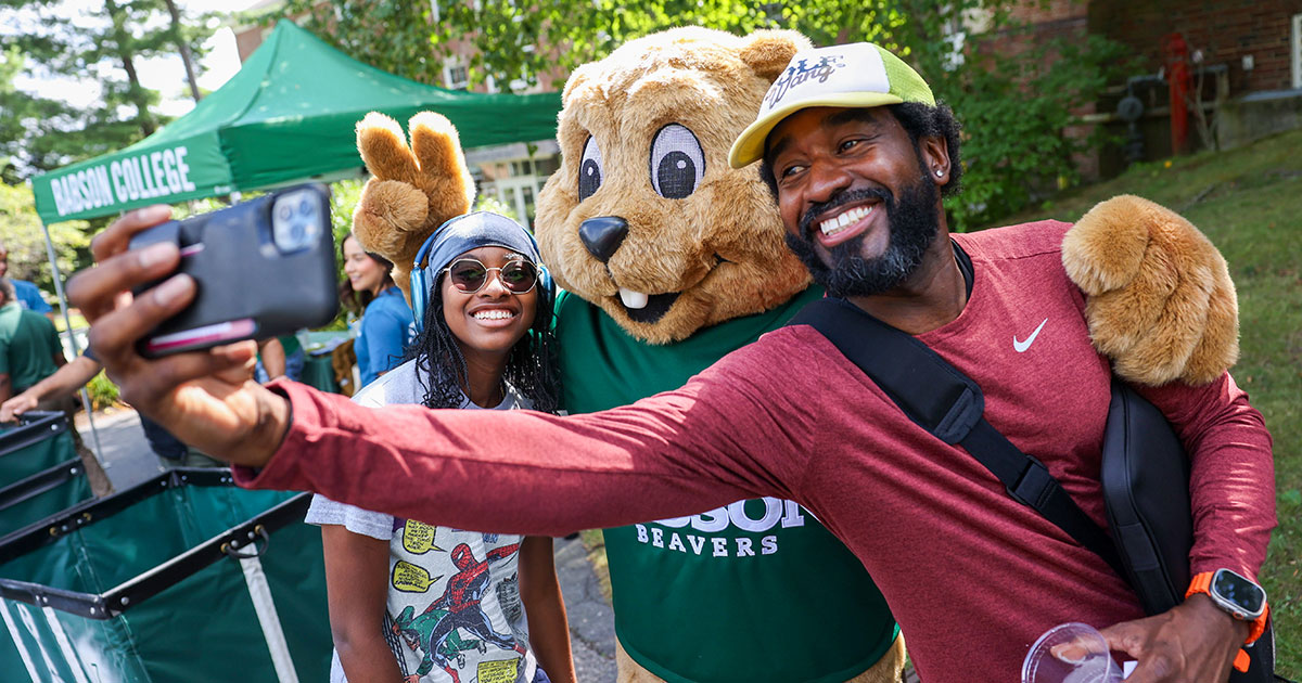 A father and daughter pose for a picture with Babson’s mascot, Biz E. Beaver