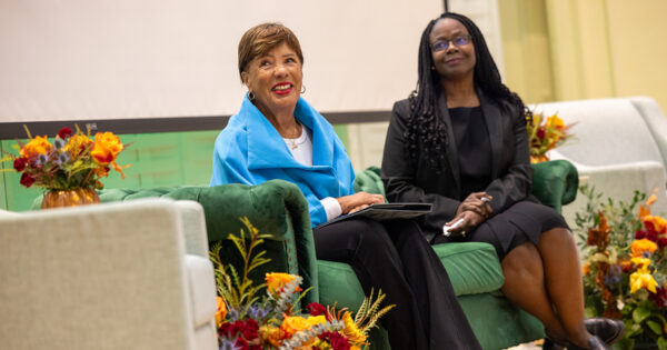 Jane Edmonds and Donna Levin listen to the keynote address while sitting on stage