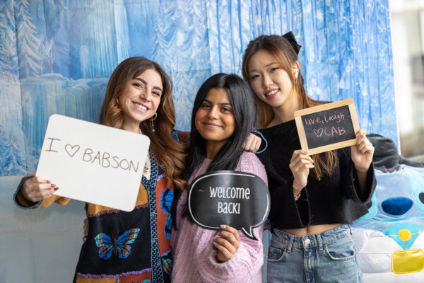 Three students hold signs to welcome back students to the start of the semester