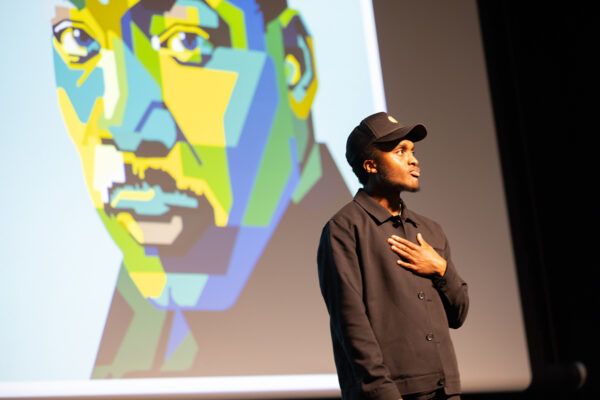 Wes Woodson puts his hand over heart with an illustration of Martin Luther King Jr. in the background