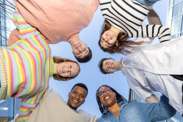 Six scholarship students form a circle and look down at the camera