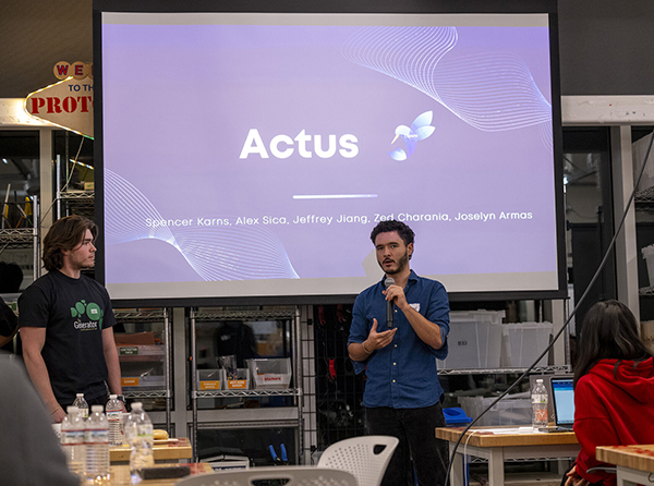 A student speaks in front of a large video screen