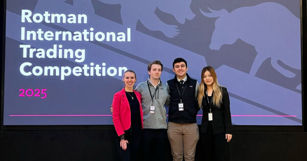 Four students pose for a photo in front of a large screen