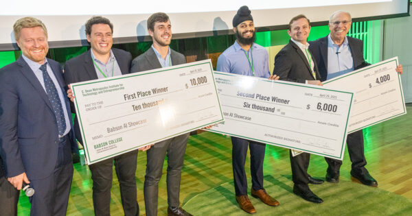 The winners stand on stage in a line holding their prize checks