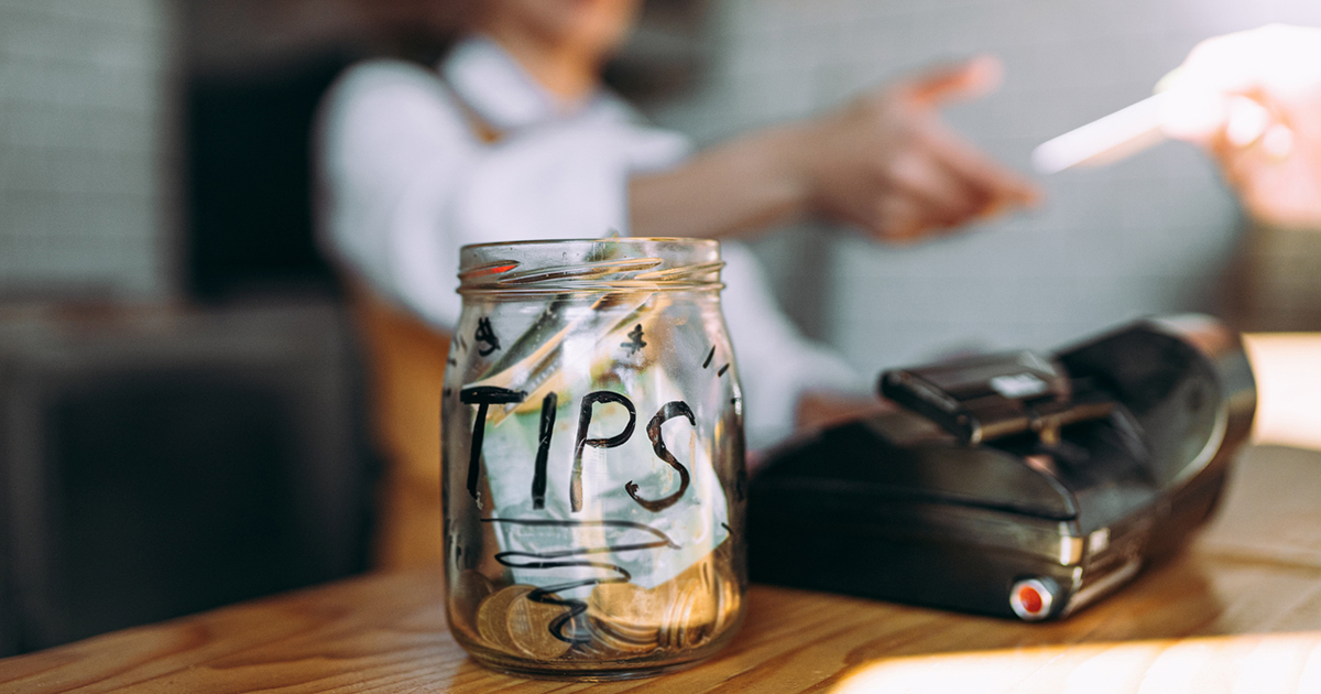 A clear tip jar with cash sits on a counter