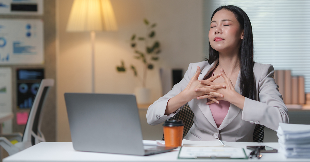 Businesswoman practices deep breathing exercise at workplace desk