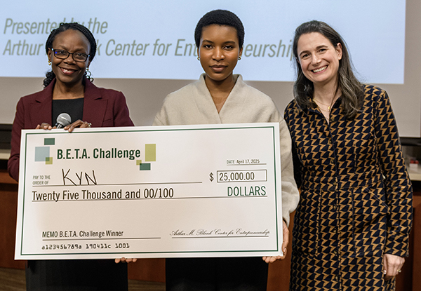 Three women pose for a photo while holding a giant check