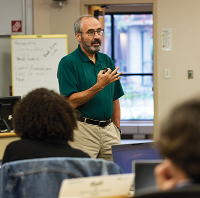 Andrew Zacharakis motions while teaching in a classroom