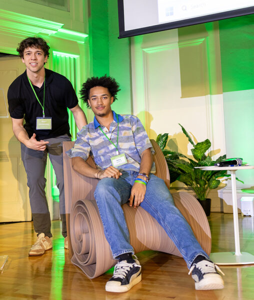 Two students pose for a photo with their AI creation, the Dam Chair