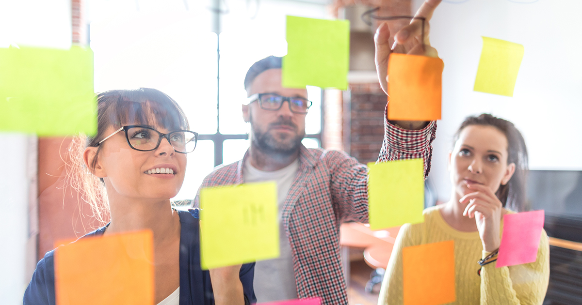 Three creative business people look at a window filled with post-it notes