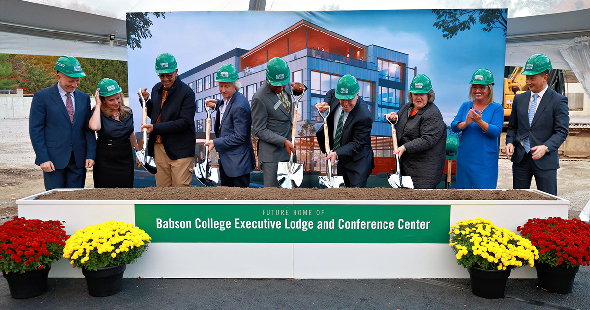 Wearing Babson-branded hard hats, nine people gather to break ground ceremonially